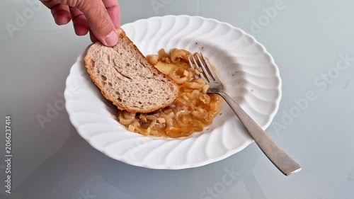 Simple homemade meal featuring slices of bread served with onion mixed in tomato sauce on a white plate. Everyday food preparation concept with rustic ingredients and casual dining