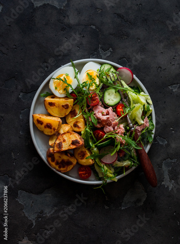 Healthy lunch - salad with tuna, vegetables, boiled egg and baked potatoes on a dark background, top view