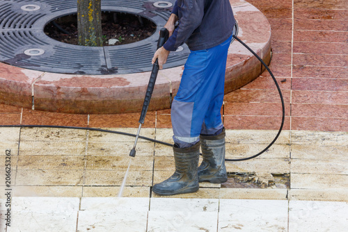 Obraz na plátně Worker cleans tiled pavement with high-pressure hose