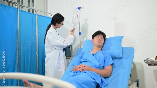 Female doctor adjusting an IV drip for a young male patient resting in a hospital bed. Professional healthcare and medical treatment