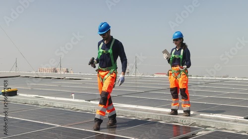 Two solar technicians inspecting rooftop photovoltaic panels, one adjusting panel alignment while colleague points and checks installation details.