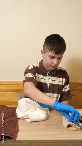 Teenager wearing gloves polishes cutlery with a towel at a table, carefully preparing clean utensils for use.