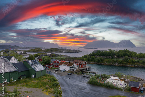 Canvas Print Traditional rorbuer sit by a narrow inlet in the Lofoten Islands, Norway, near Svolvaer or Henningsvaer, as sunset bands paint the sky above gray water and vegetation