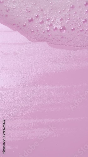 Closeup vertical soap foam texture on pink background, white shampoo slow motion