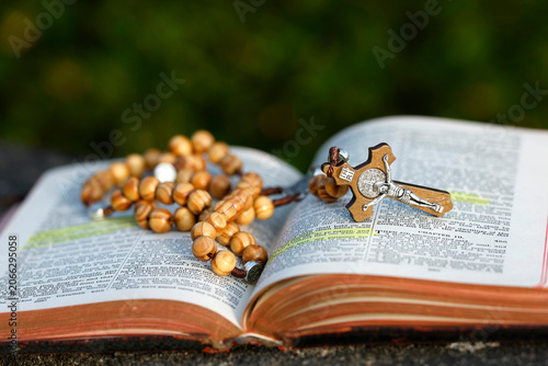 A wooden rosary adorned with a silver crucifix and medals lies open on the pages of a Bible with highlighted passages.