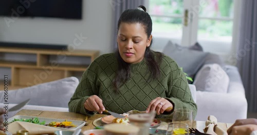 African American woman seeing pink plate cutting at table with knife, fork, lifting bite, chewing