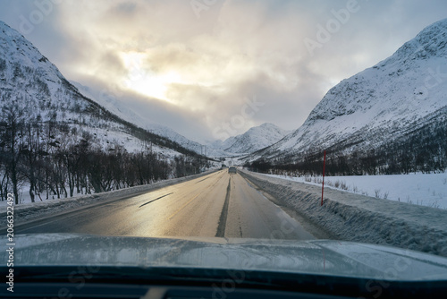 Epic POV Winter Lofoten Road Trip: Driving a Wet, Icy Highway Through a Dramatic Snow-Covered Mountain Valley in Arctic Norway, Remote Scandinavian Landscape View.