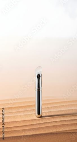 Sleek Silver Cosmetic Applicator on Textured Sandy Background with Copy Space