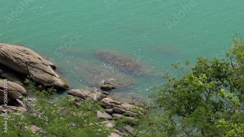 Crystal-clear turquoise waves wash over rocky shoreline along the tropical coast of Khanom, Thailand. Scenic seascape featuring dramatic cliffs, coastal vegetation, and natural beauty.