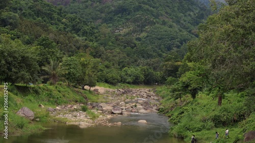 Wide view of tropical river flowing through lush mountains in southern Thailand. Visitors enjoy peaceful riverside recreation surrounded by pristine tropical nature.