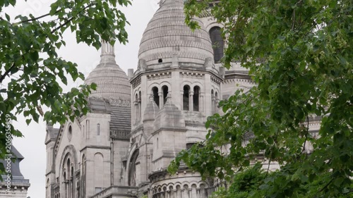 Sacre Coeur basilica church dome stands behind green tree branches in Paris France. Roman Catholic cathedral architecture represents historic European landmark tourism travel holiday trip.