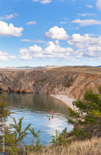 Lake Baikal in summer. People relax on the sandy beach of Olkhon Island, sunbathe and ride SUP boards in the shallow bay of the Small Sea on a sunny day in July. Active recreation in summer holidays