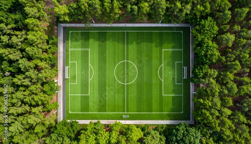 Aerial top view of green football field surrounded by trees, soccer pitch overhead view with white lines markings.
