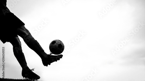Silhouette of a soccer player's legs and foot controlling a football against a bright sky, showcasing athletic skill and movement.
