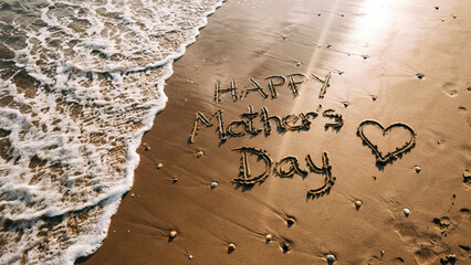 Heartfelt Mother's Day message "Happy Mother's Day" lovingly written in golden beach sand with gentle ocean waves softly approaching
