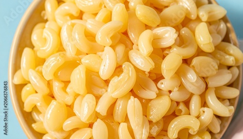 Close-up bowl of cooked elbow macaroni pasta, glossy yellowish texture, plain without sauce, light blue background contrasting pasta color, simple composition highlighting shape and food ingredient de