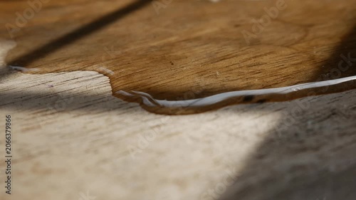 Macro close-up of thin water stream trickling across rustic aged wood grain surface with warm golden light and shadow in still life photography