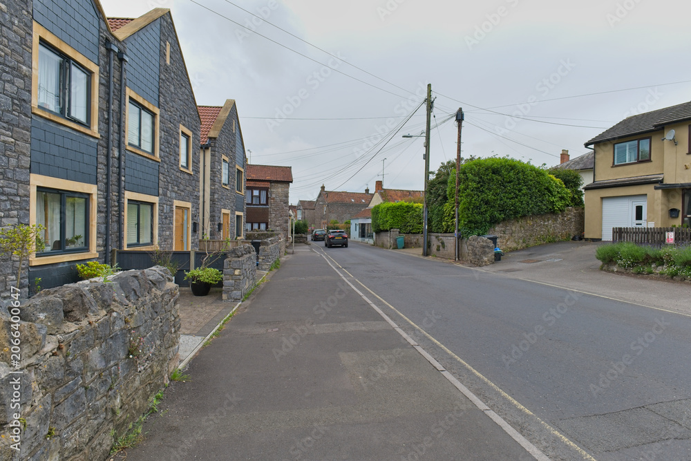 Obraz premium A scenic village street features modern dark-sided homes with stone walls on the left in the village of Cheddar - Somerset - UK