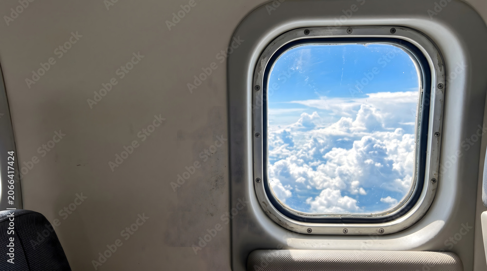 Fototapeta premium Airplane window view above clouds with bright sky and minimal cabin interior copy space composition