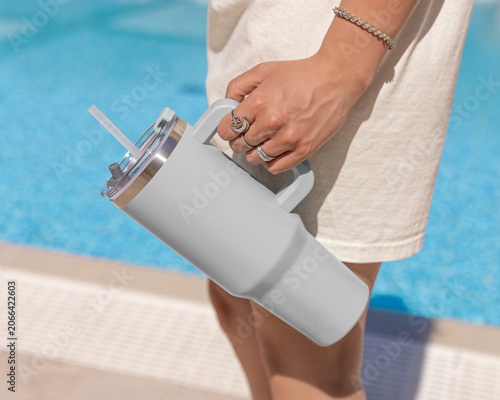 Blank grey 40oz tumbler mockup, young woman at poolside, hand close up. Lifestyle scene