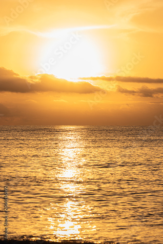 Tranquil Beach Sunrise: Calm Waters, Cloudy Sky, Sun Peeking Through