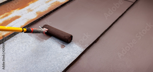 painting tin metal roof with roller and brown paint. rusty house roofing restoration