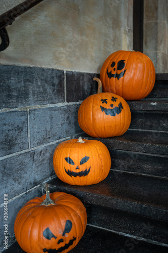 Foto Four orange pumpkins with painted spooky faces arranged on dark stone staircase steps for Halloween