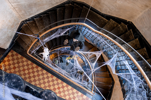Obraz na plátne Overhead view of a vintage spiral staircase draped with white cobwebs and hanging Halloween figures over a checkered floor
