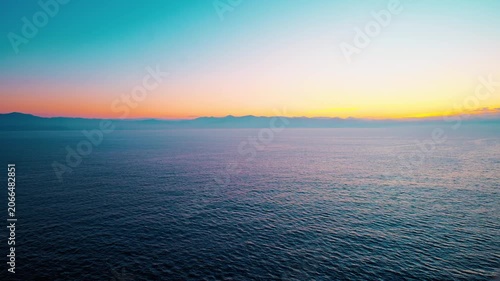 Sunrise over calm ocean with distant mountain horizon
