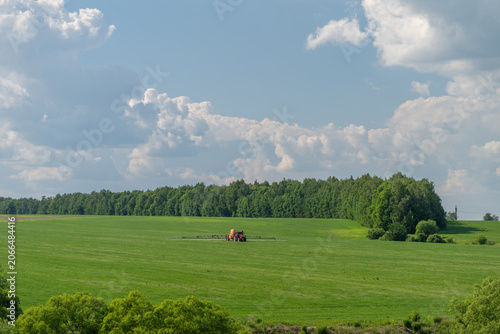Fotografie Tractor working in expansive green field under a blue sky