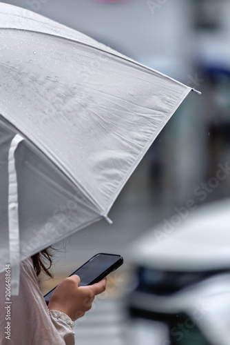 Close-up of pedestrian with transparent umbrella using a smartphone on a rainy urban street.