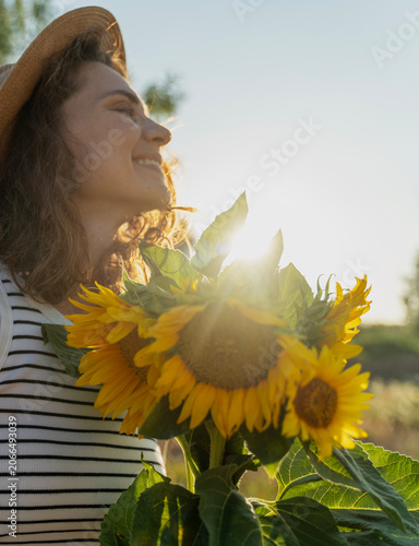Side profile portrait of a young woman pressing sunflowers to her chest in a field at sunset