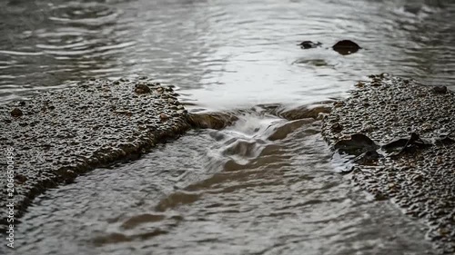 Rainwater flows through a broken asphalt road during a heavy storm