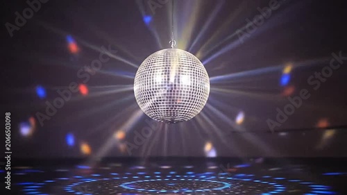 A sparkling silver disco ball reflects vibrant light rays in a dark nightclub setting