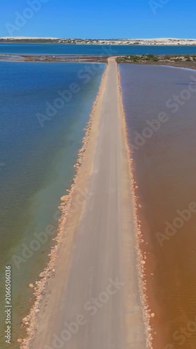 Vertical aerial drone shot flying low along the central road of Point Sinclair Pink Lake, rising to reveal the blue and pink lakes on both sides