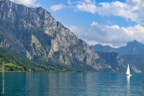 White Sailboat Gliding Past Majestic Traunstein Mountain On Traunsee Lake