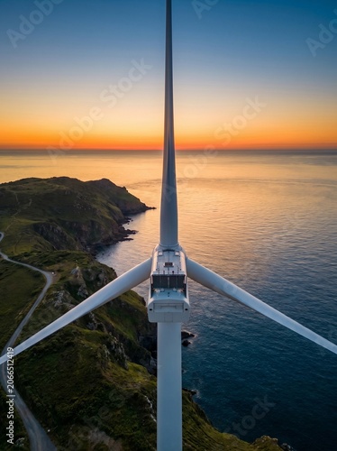 Aerial view of offshore wind turbine at sunset over ocean and coastal landscape with symmetrical composition. Copy space