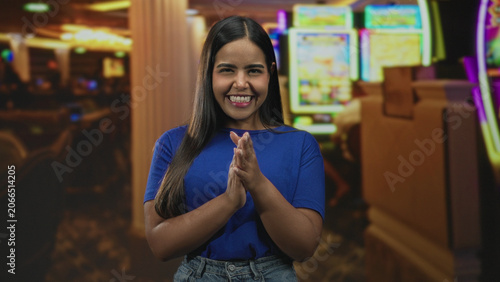 Tableau sur toile Woman claps hands by brightly lit slot machines in casino building interior wearing blue shirt, smiling with closed eyes; celebration joy