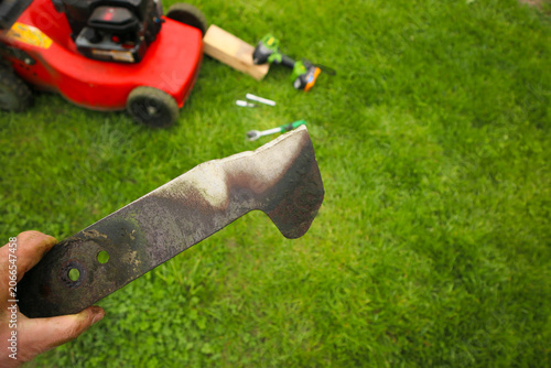 Man holding a worn dull lawn mower blade close up on a green grass background