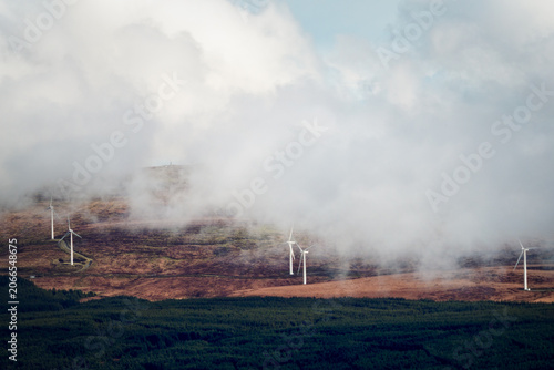 Wind turbines are visible on a barren landscape partially obscured by clouds.