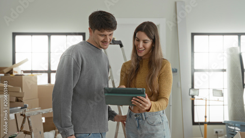 Konstfotografi Man and woman high five while holding a tablet amid stacked moving boxes, a stepladder and work lights in a bright building room; new home joy