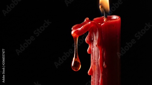 Close-up of a red candle with melting wax dripping down against a dark background with cinematic lighting.