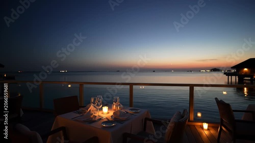 Romantic candlelit dinner setting at an overwater restaurant during a beautiful twilight sunset.