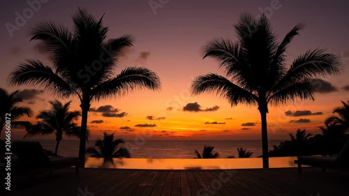Stunning tropical sunset view over a luxury infinity pool with silhouette palm trees.