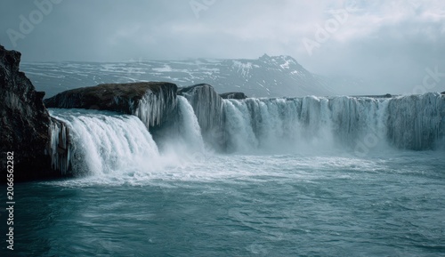 Majestic Waterfall Cascading into Turquoise Waters Under a Moody Sky.