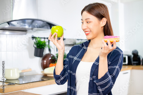 Obraz na płótnie Young Asian woman hesitating between choosing a healthy apple and sweet donut