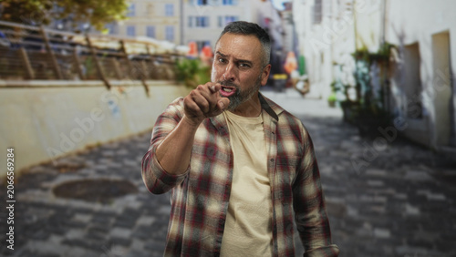 Foto Man with grey beard points finger down a cobblestone street beside a building, forearm exposed; anger confrontation