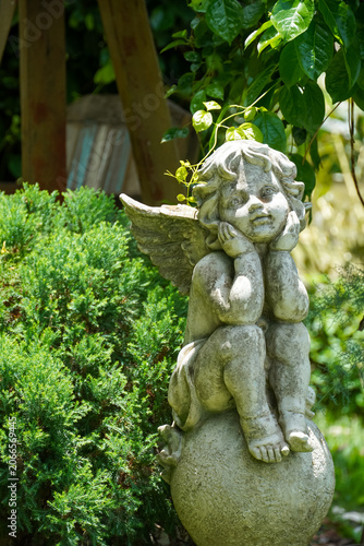 Stone cherub statue resting on a spherical base amidst lush green foliage