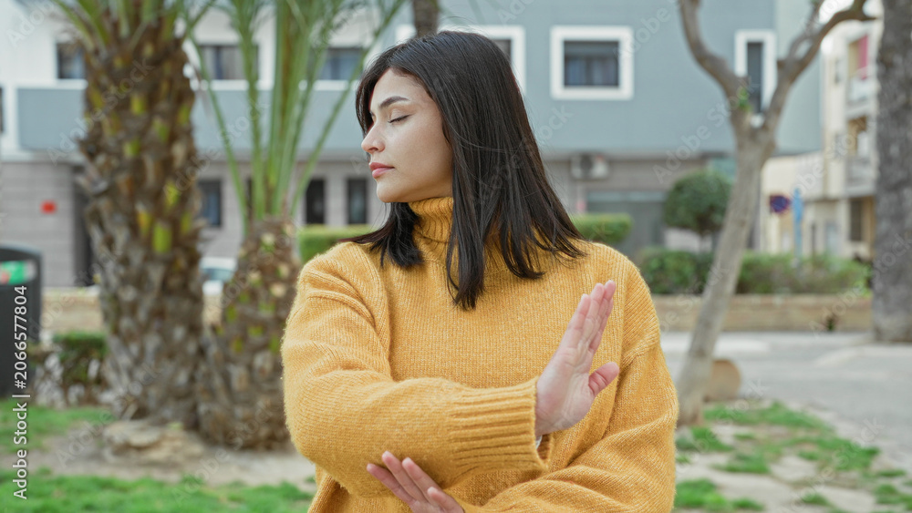 Fototapeta premium Woman shows palm forward stop gesture on street wearing yellow turtleneck sweater; boundary assertiveness determination.