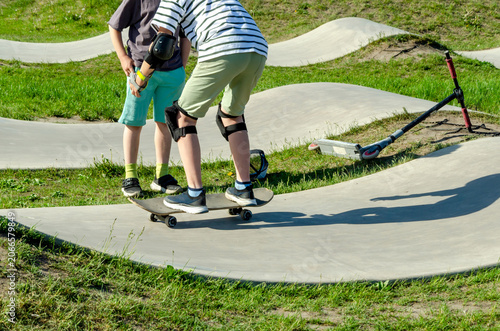 teen rides skateboard on concrete pump track while friend watches. learning to ride skateboard builds skills. this skateboard offers outdoor recreation and friendship for youth today.